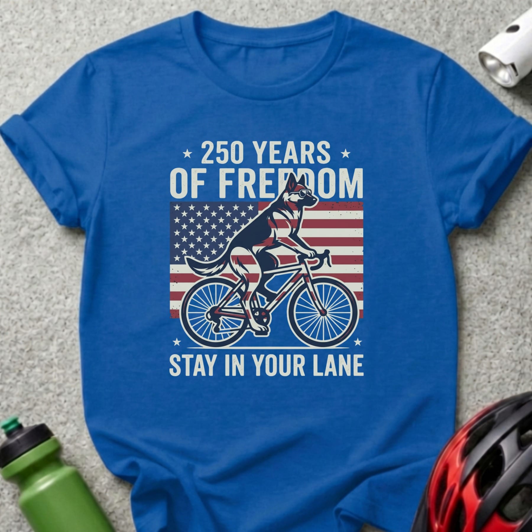 Blue t-shirt with a dog on a bicycle in front of the American flag, text reads "250 YEARS OF FREEDOM STAY IN YOUR LANE".