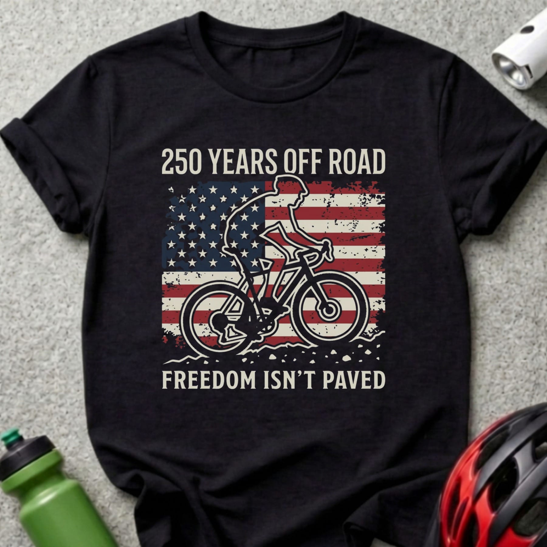 Black t-shirt with cyclist silhouette on American flag, "250 Years Off Road Freedom Isn't Paved".