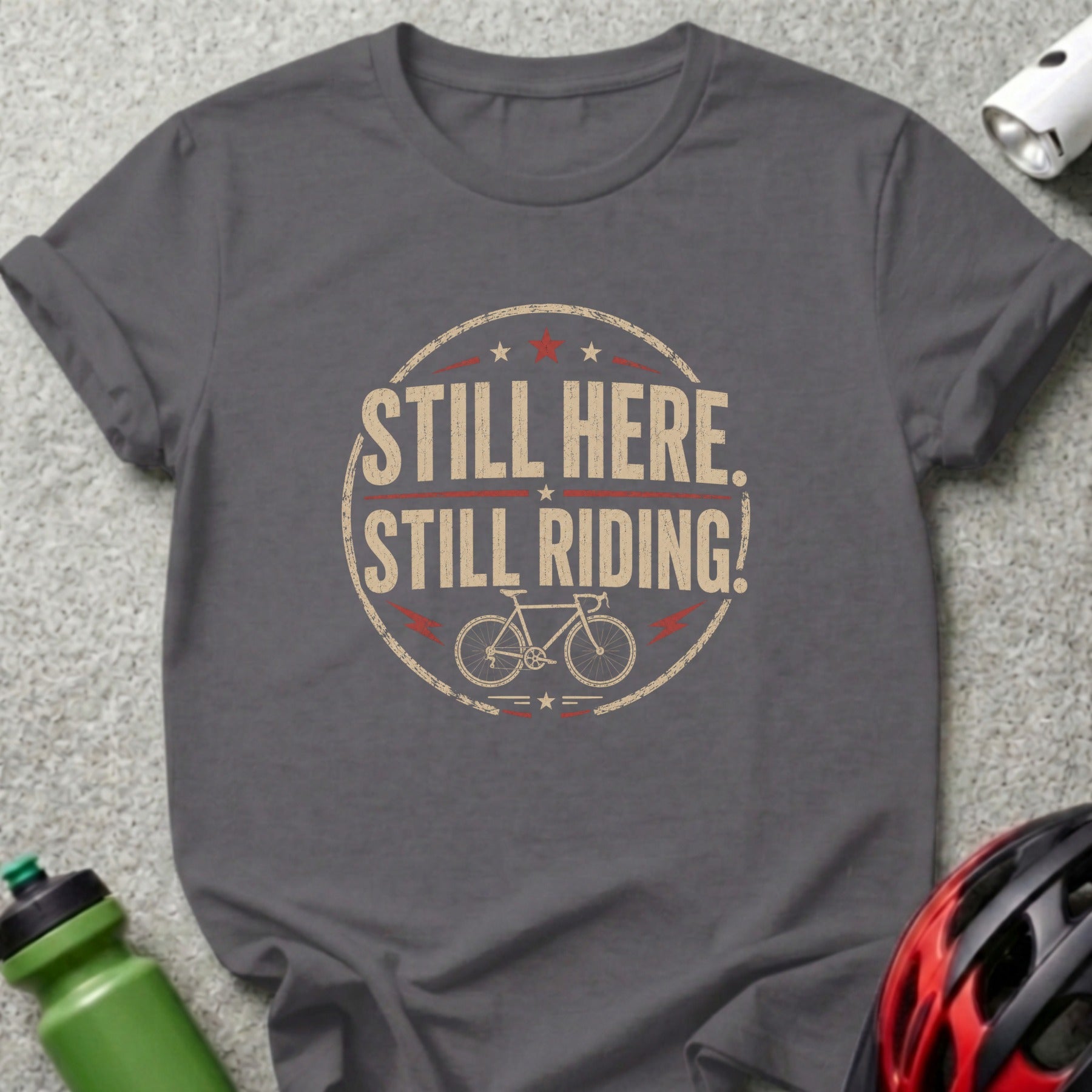 Grey t-shirt with "STILL HERE. STILL RIDING!" and bicycle graphic.