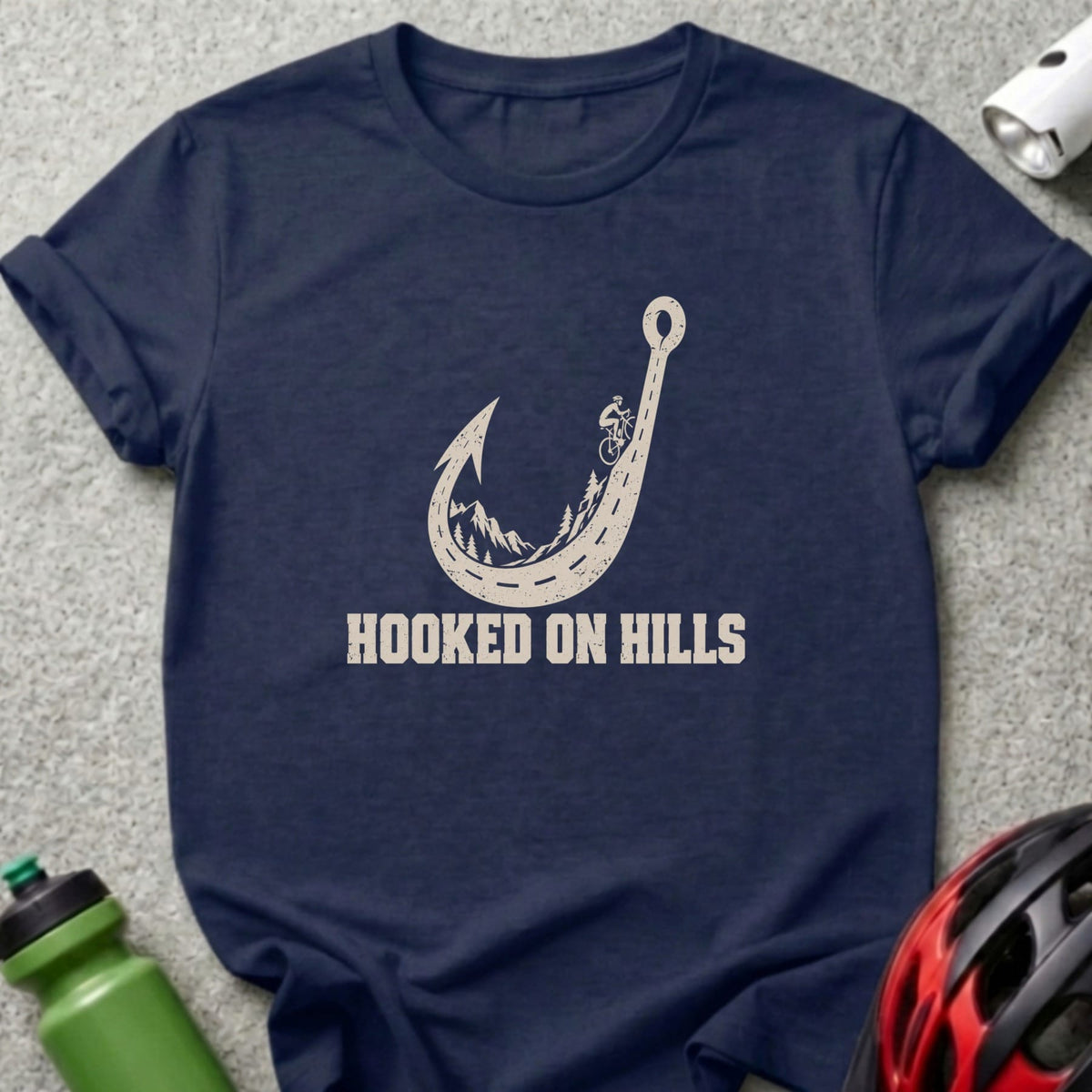 A navy blue t-shirt printed with a fishhook-shaped winding road graphic and the text "HOOKED ON HILLS".