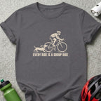 A charcoal gray t-shirt with a cream-colored graphic of a cyclist and a dachshund, accompanied by the text "EVERY RIDE IS A GROUP RIDE".