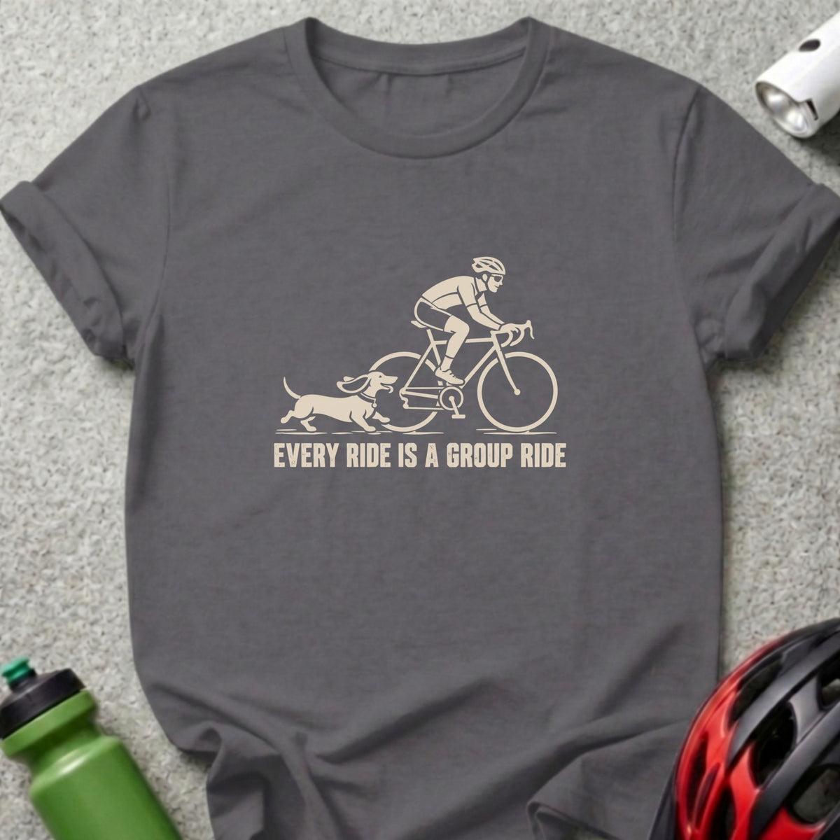 A charcoal gray t-shirt with a cream-colored graphic of a cyclist and a dachshund, accompanied by the text "EVERY RIDE IS A GROUP RIDE".