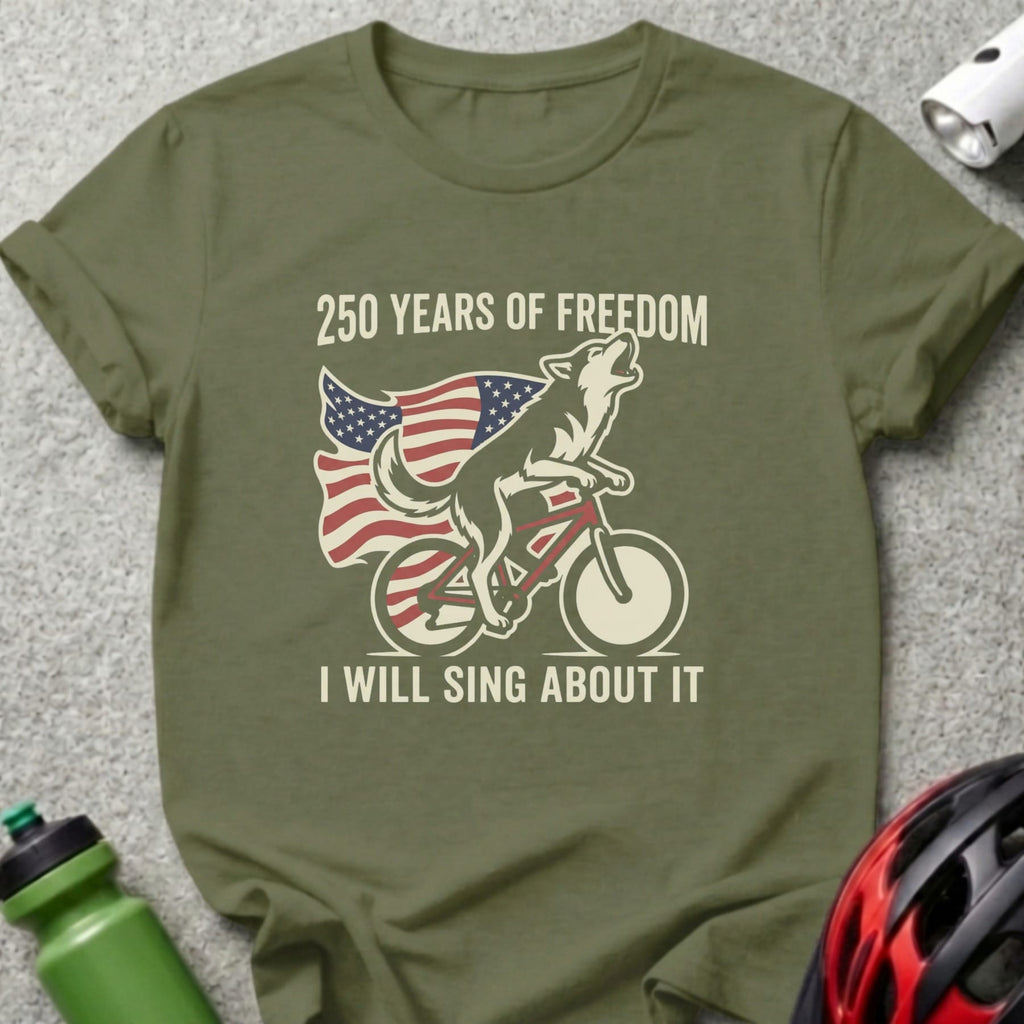 Olive t-shirt with a wolf on a bicycle under the American flag, text reads "250 Years of Freedom I Will Sing About It".