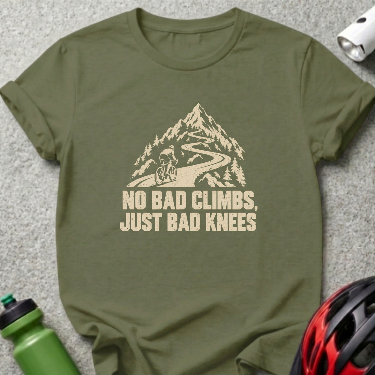 Olive green crew neck t-shirt featuring a graphic of a cyclist climbing a mountain road with the text NO BAD CLIMBS, JUST BAD KNEES.