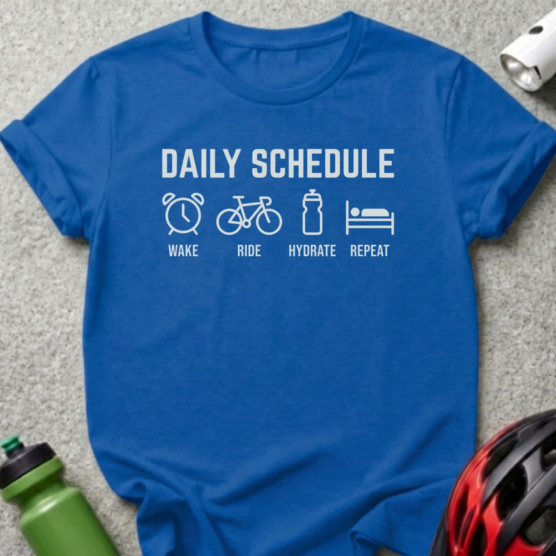 Blue t-shirt with "Daily Schedule: Wake, Ride, Hydrate, Repeat" text and icons.