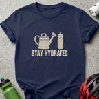 A dark blue t-shirt with a white graphic of a watering can, water bottle, and the text STAY HYDRATED.