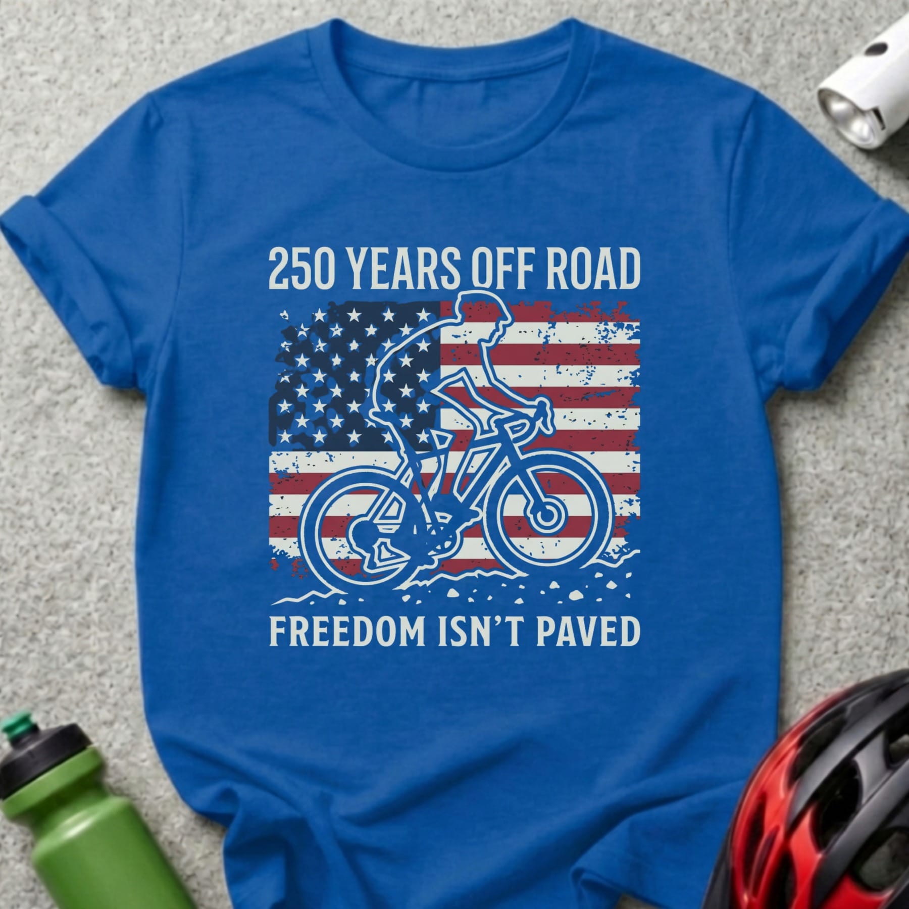 Blue t-shirt with cyclist and American flag, "250 Years Off Road Freedom Isn't Paved".