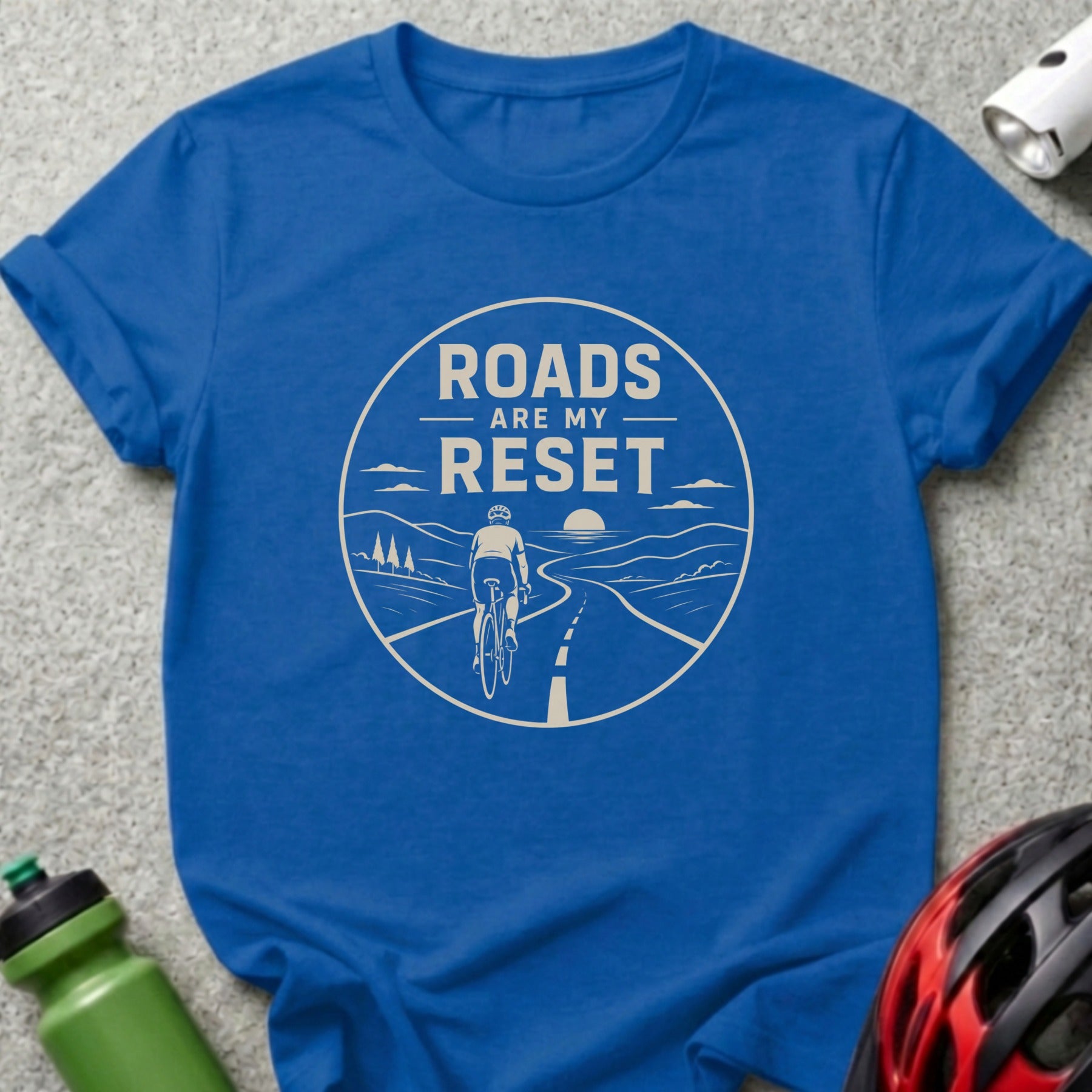 Blue t-shirt with a graphic of a cyclist on a road with the text "Roads Are My Reset".
