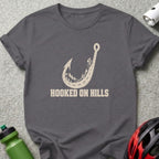 Dark gray t-shirt featuring a fishing hook shaped like a mountain road, with text reading HOOKED ON HILLS.