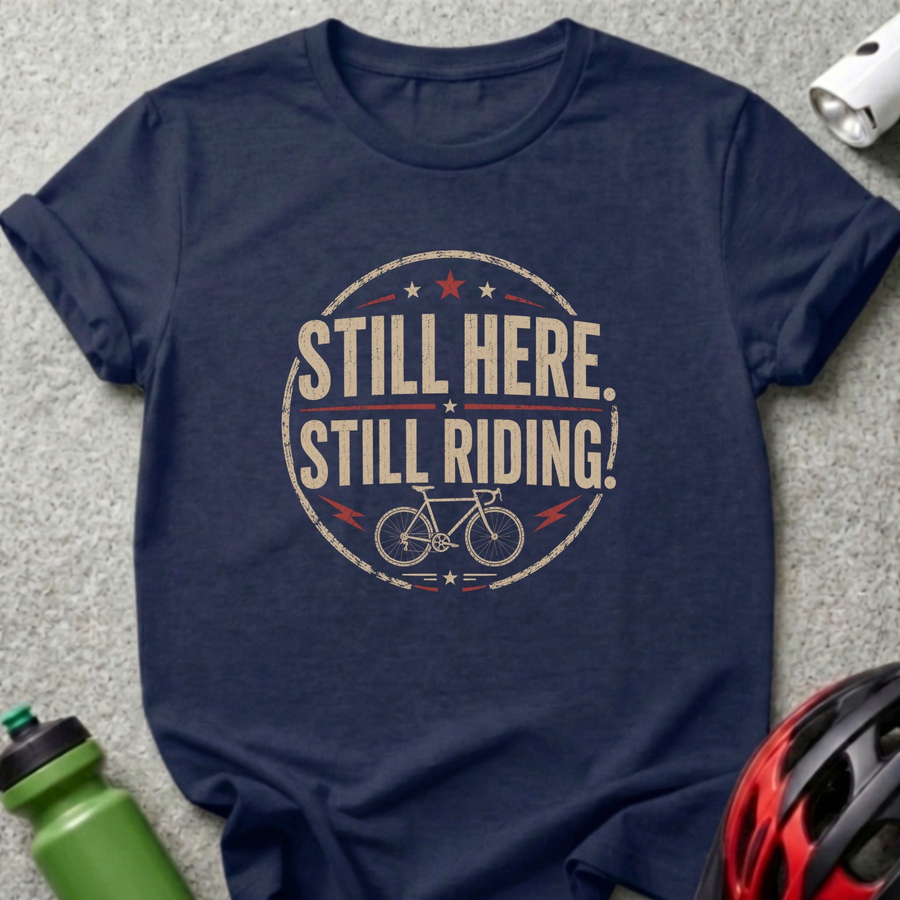 Navy t-shirt with distressed circular graphic: "STILL HERE. STILL RIDING!" and a bicycle.
