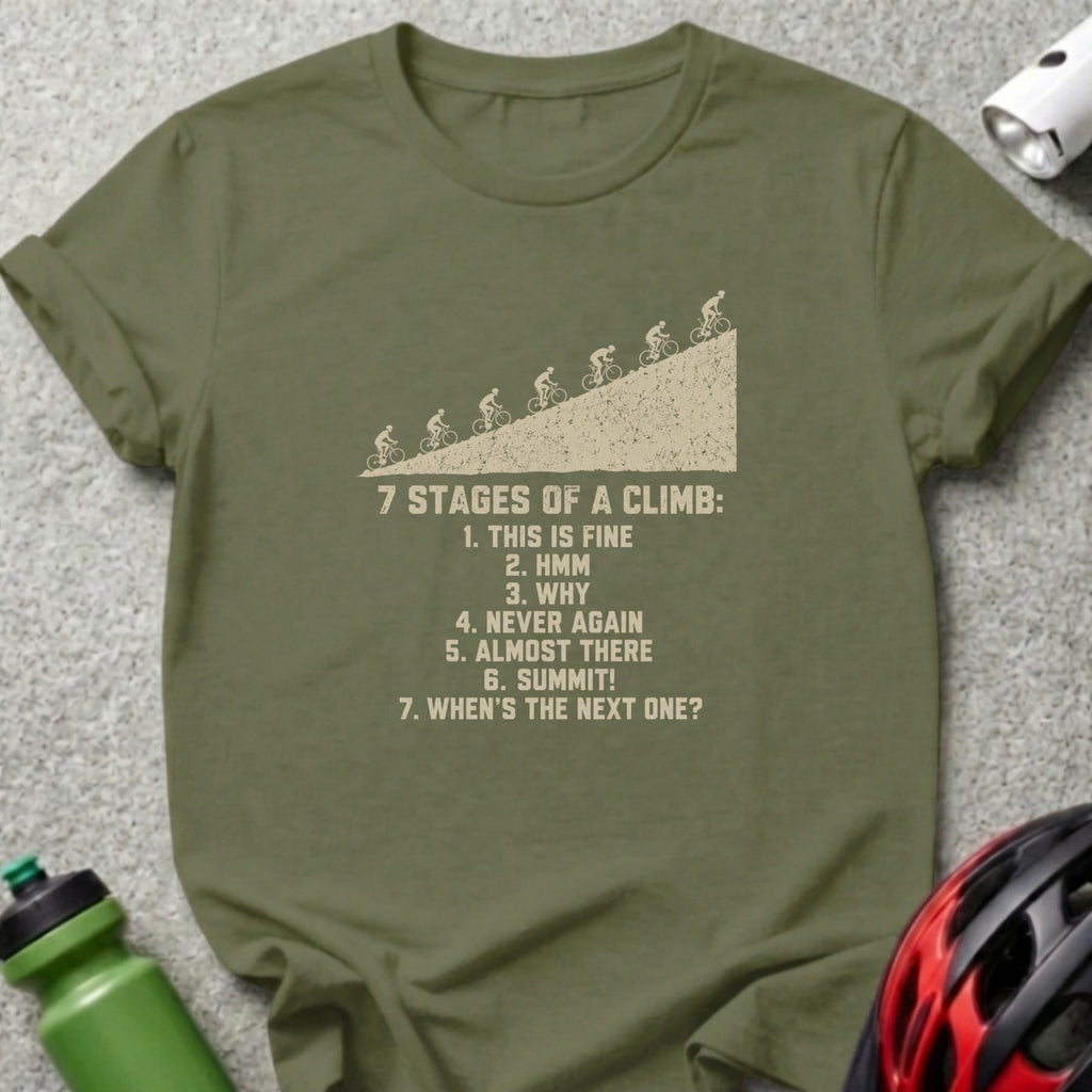 An olive green t-shirt featuring a graphic of cyclists climbing a hill and text listing the seven stages of a climb.