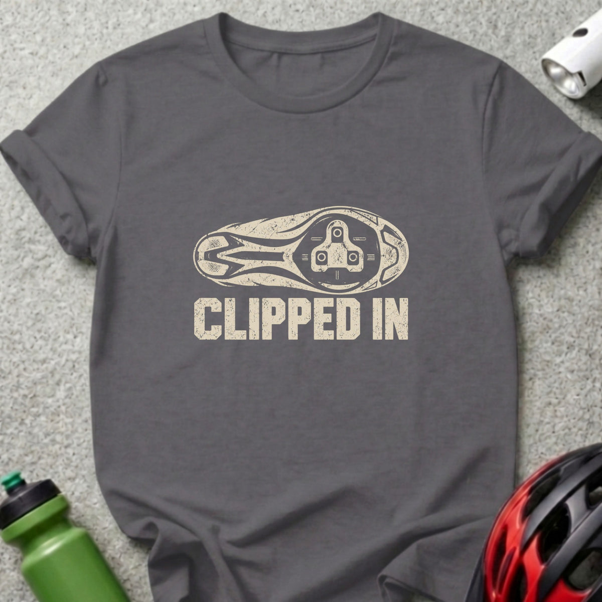 A charcoal gray t-shirt with a distressed graphic of a bicycle cleat and the text CLIPPED IN.