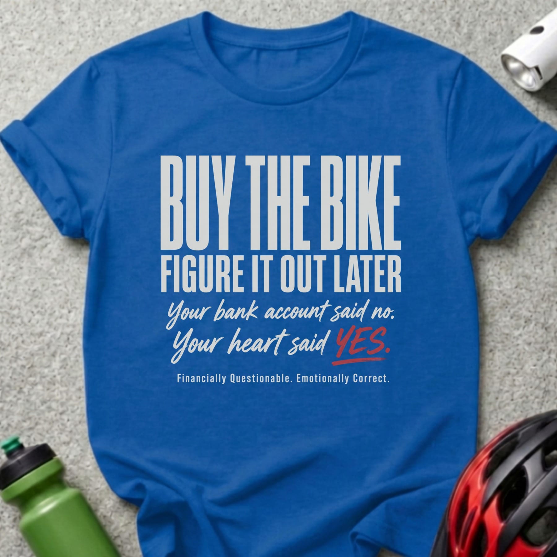 Blue t-shirt with text: "Buy the Bike, Figure It Out Later. Your bank account said no. Your heart said YES. Financially Questionable. Emotionally Correct."