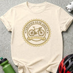 Cream t-shirt with "Certified Gear Addict" circular logo and bicycle graphic.
