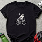 Black t-shirt with a white graphic of an owl riding a bicycle under a crescent moon.