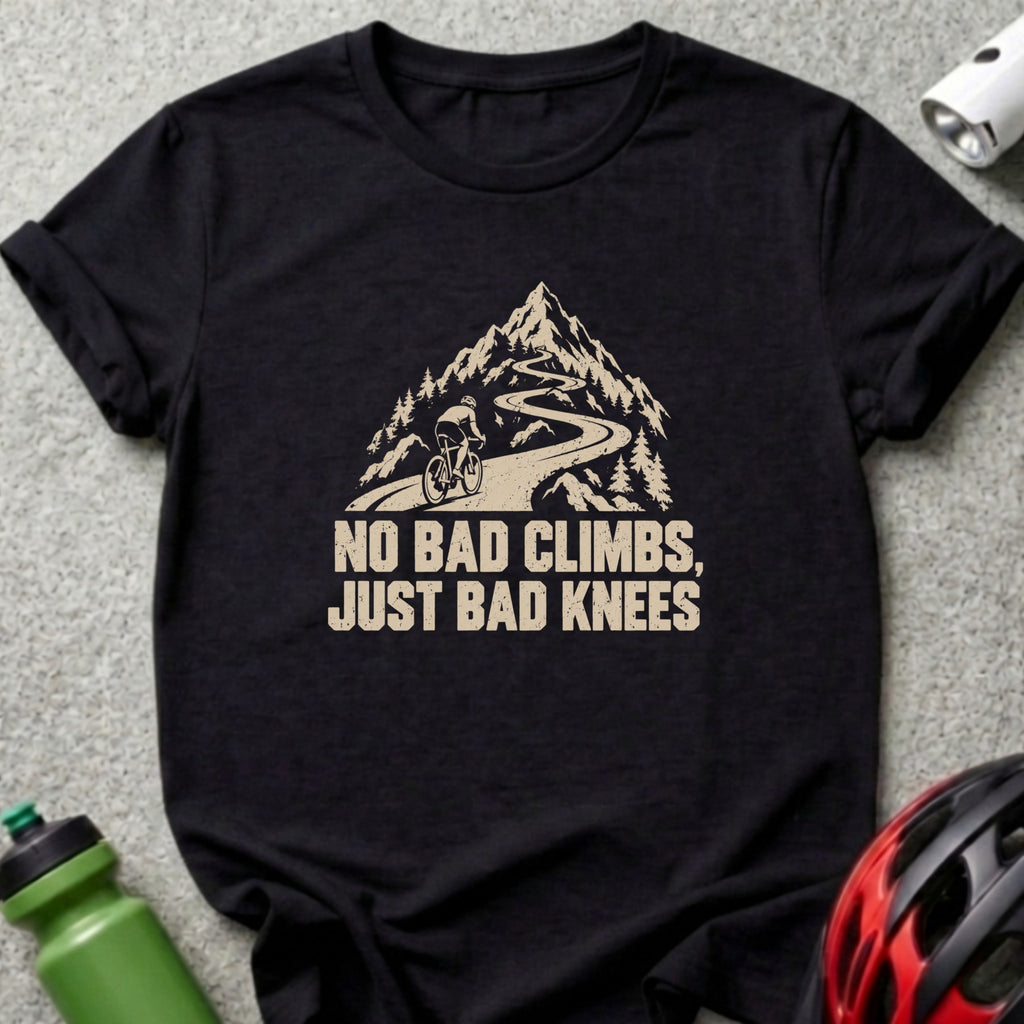 A black t-shirt printed with a graphic of a cyclist climbing a mountain road and text reading NO BAD CLIMBS, JUST BAD KNEES.