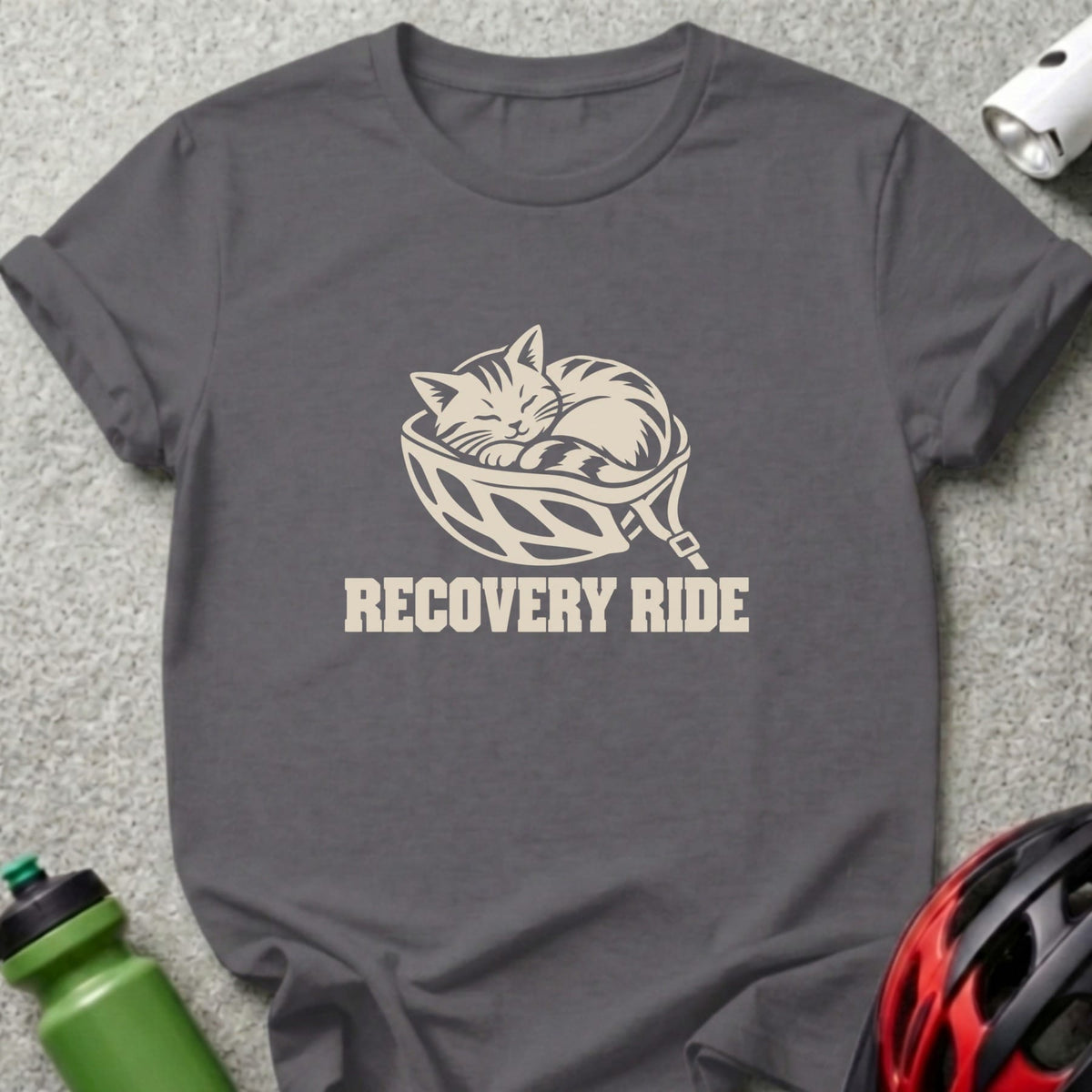 A dark gray crewneck t-shirt featuring a graphic of a sleeping cat inside a bicycle helmet and the text "RECOVERY RIDE".
