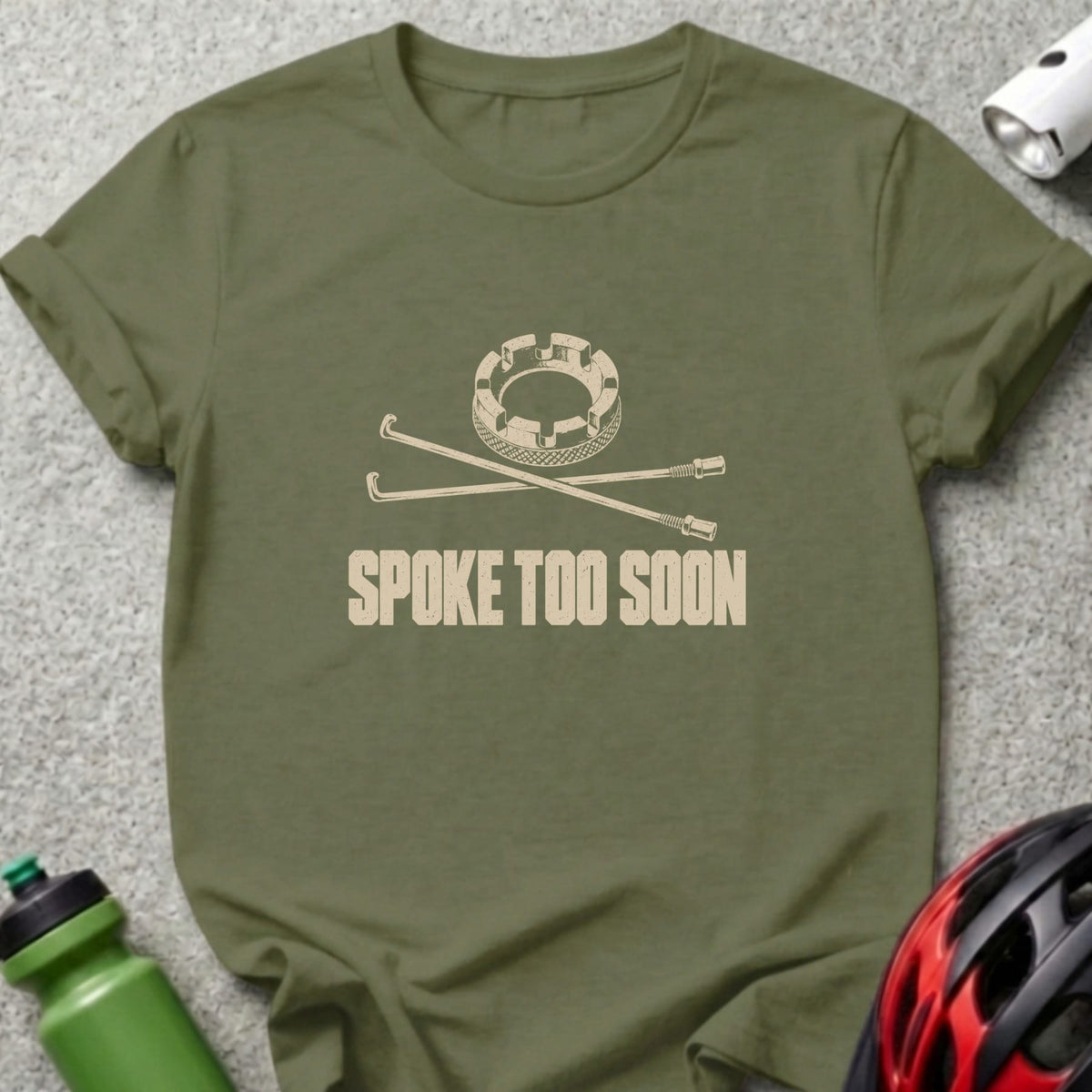 An olive green t-shirt with a bicycle wheel graphic and the text SPOKE TOO SOON.